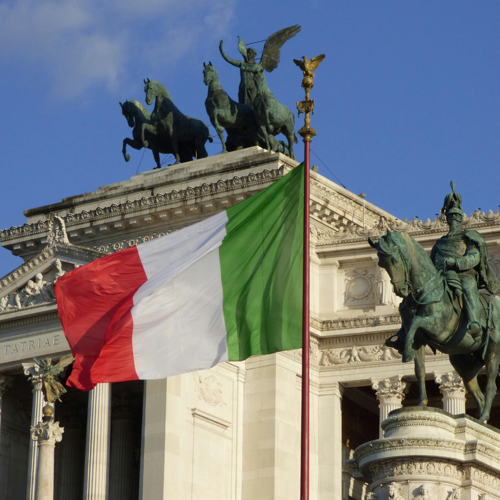 Die italienische Flagge vor dem Vittoriano in Rom, mit der bronzenen Quadriga vor blauem Himmel