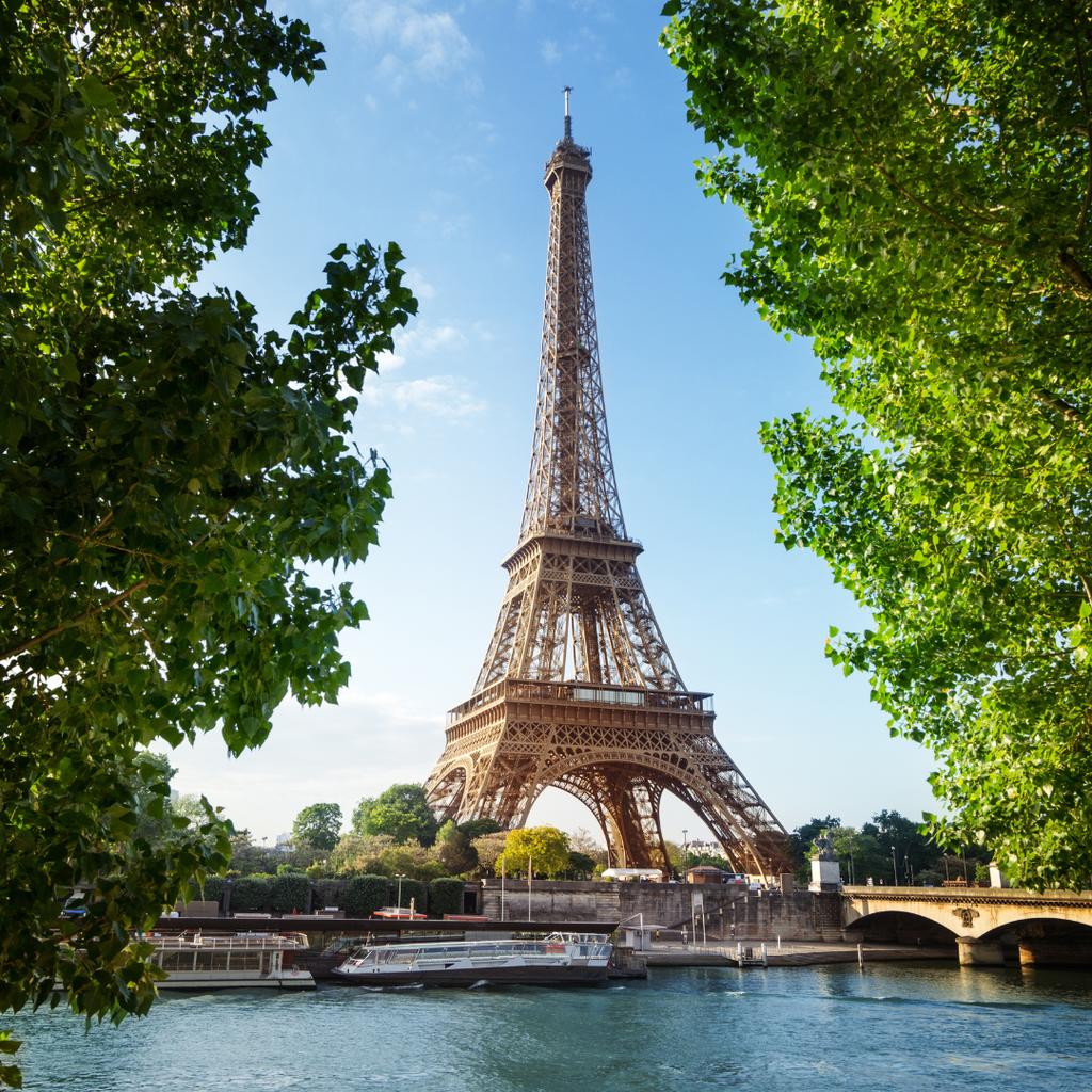 Der Eiffelturm über der Seine, gerahmt von Platanenlaub, mit Ausflugsbooten am Kai